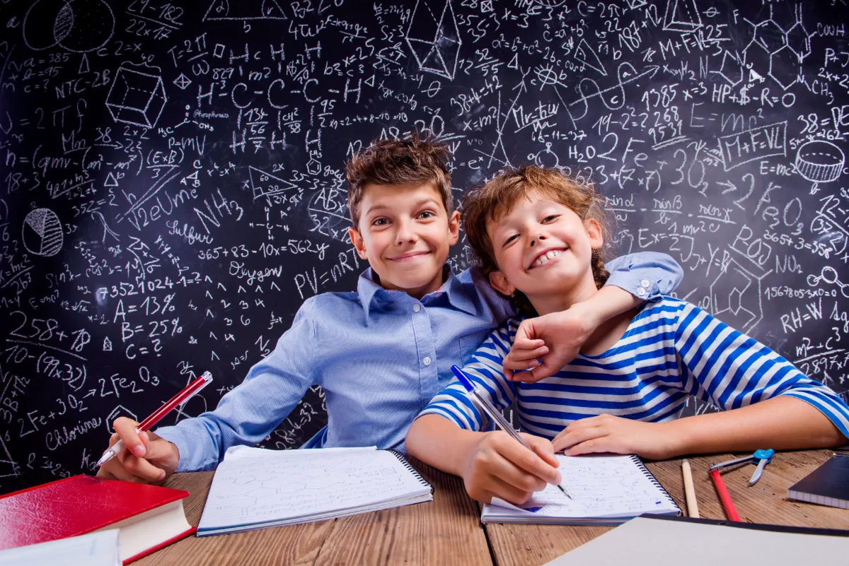 Zwei fröhliche Kinder lernen gemeinsam Mathe vor einer Tafel mit Formeln – Mathe-Nachhilfe in Karlsruhe-Durlach